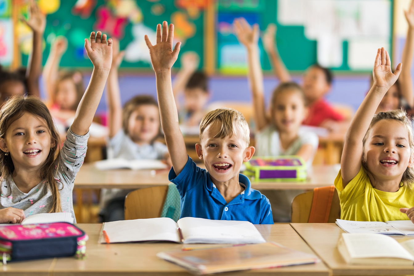 Happy school kids raising hands on a class in the classroom.